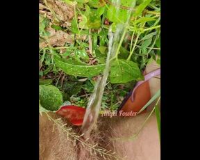 Village woman in a red tunic is pissing in the middle of a green field